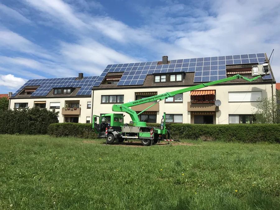 Grüner LKW-Hubsteiger von Solarreinigung Bayreuth vor einem Mehrfamilienhaus mit Photovoltaik-Dach